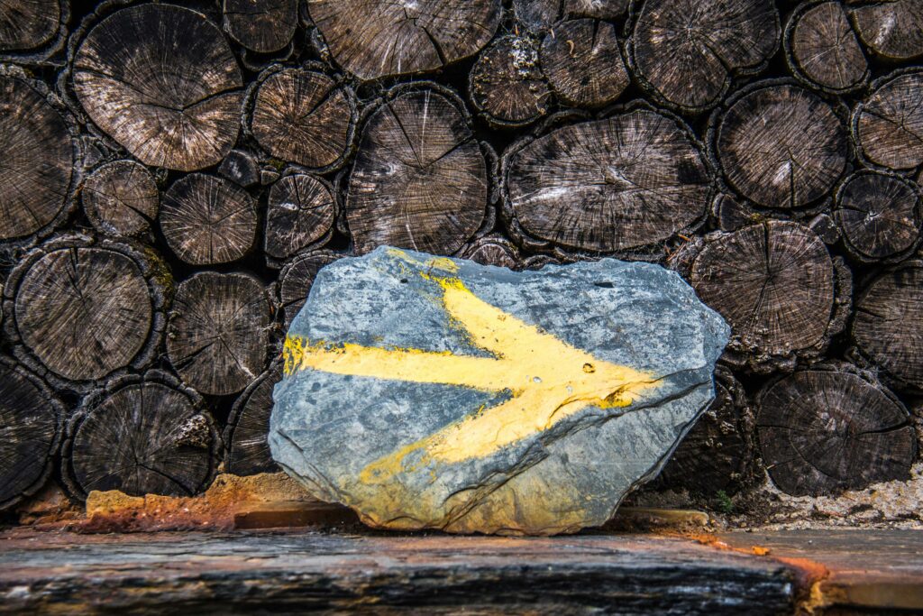 Close-up of a painted rock with a yellow arrow placed before a stacked timber backdrop.